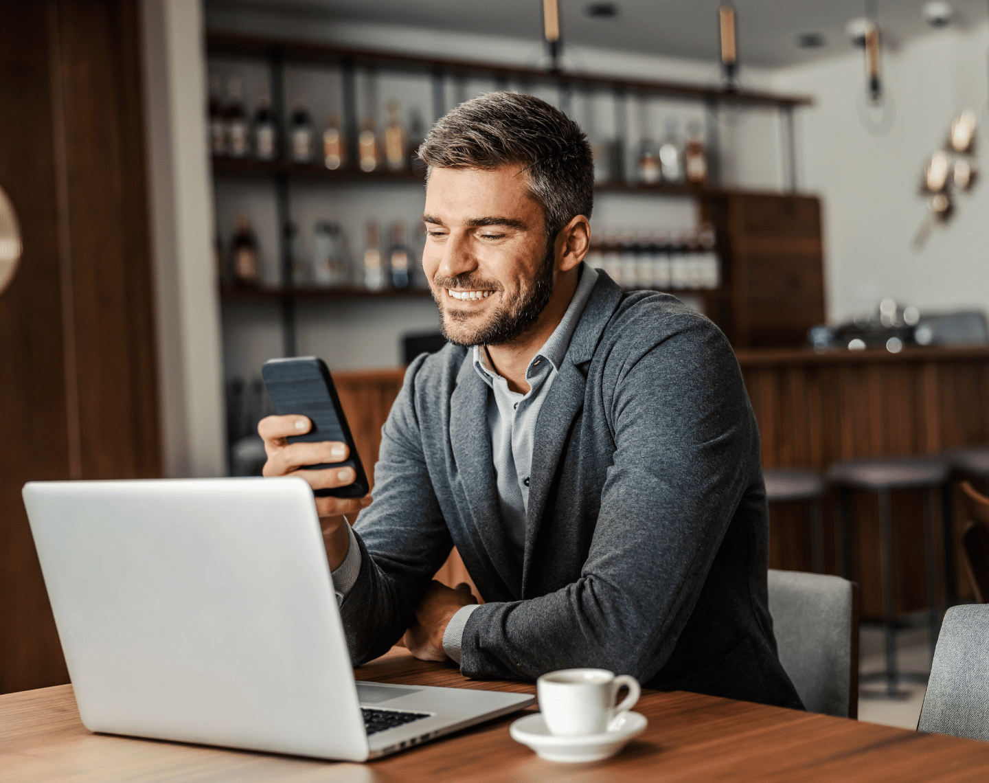 Man Looking at Phone and Laptop in Coffee Shop
